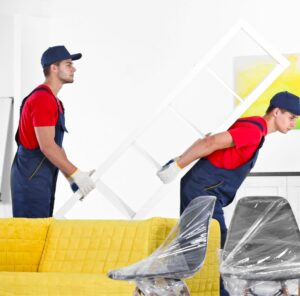 Umzug in Kaiserslautern Zwei Helfer tragen ein Möbelstück an einem gelben Sofa vorbei – Umzug in Kaiserslautern